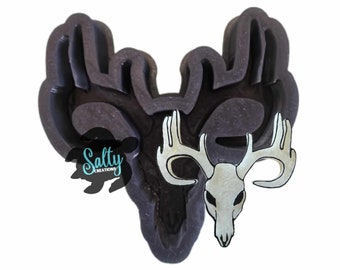 May include: A black silicone mold of a deer head with antlers. The mold is designed to create a cookie or cake topper. The mold is shown with a white deer skull with antlers.