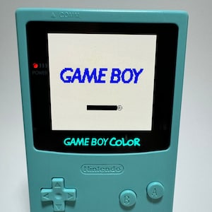 May include: A teal Game Boy Color handheld video game console with a black and white screen displaying the text "GAME BOY" and "GAME BOY COLOR". The console has a black Nintendo logo, black buttons, and a speaker grill.