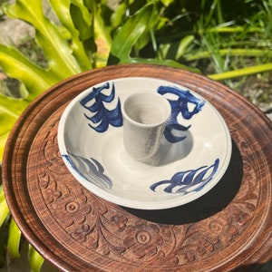 May include: A white ceramic candle holder with a blue and white floral design. The holder has a small dish on the bottom and a tall, cylindrical center piece for a candle.