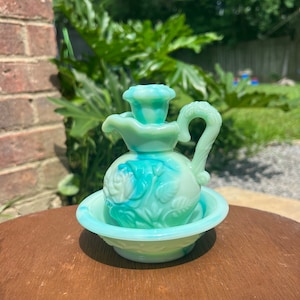 Puede incluir: Un juego vintage de jarra y cuenco de vidrio verde con un diseño floral. La jarra tiene un asa y un pico, y el cuenco es redondo con un borde festoneado.