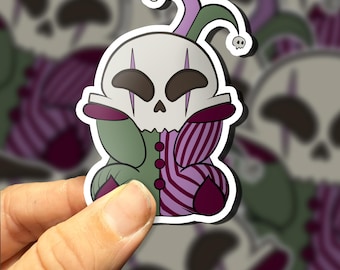May include: A sticker of a cartoon skull wearing a jester's hat and a purple and green striped costume. The skull has a white face with black eyes and a black mouth.