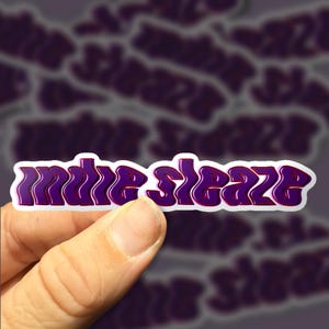 May include: A white sticker with the text "indie sleaze" in a purple and red wavy font.