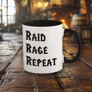 Puede incluir: Una taza de café blanca con interior y asa negros. La taza presenta las palabras "RAID RAGE REPEAT" en negro, con letras de estilo gótico. La taza está sobre una mesa de madera rústica.