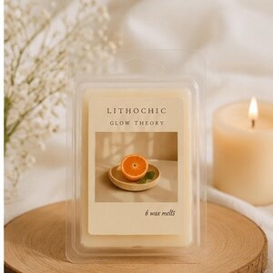 May include: A clear plastic package containing six wax melts, with the text "LITHOCHIC GLOW THEORY". The label features an image of an orange slice on a small plate. A lit candle and a wooden coaster are also in the image.