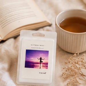 May include: A white wax melt package with the text "LITHOCHIC - SACRED SPACE" and an image of a person doing yoga at sunset. A cup of tea, an open book, and dried flowers are also in the image.