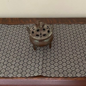 May include: A small, ornate bronze incense burner with a decorative top sits on a black and white patterned table runner.