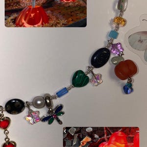 May include: A silver chain necklace with various charms, including a dragonfly, a heart, a star, and a small pumpkin. The necklace is accented with colorful beads, including blue, green, red, and orange.