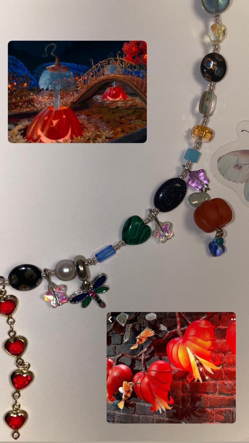 May include: A silver chain necklace with various charms, including a dragonfly, a heart, a star, and a small pumpkin. The necklace is accented with colorful beads, including blue, green, red, and orange.