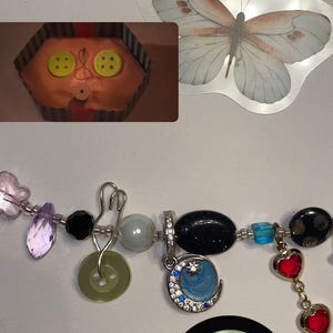 May include: A colorful charm bracelet with a variety of charms, including a crescent moon charm with blue and white enamel, a green button charm, a black bead charm, and a red heart charm.