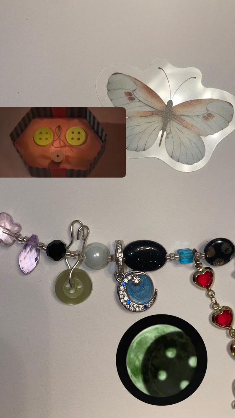 May include: A colorful charm bracelet with a variety of charms, including a crescent moon charm with blue and white enamel, a green button charm, a black bead charm, and a red heart charm.