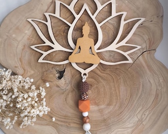 May include: Wooden wall hanging featuring a lotus flower design with a seated Buddha figure in the center. The hanging includes a string of beads in various colors and shapes, and a clear crystal at the bottom. The overall color scheme is natural wood tones and earth tones.