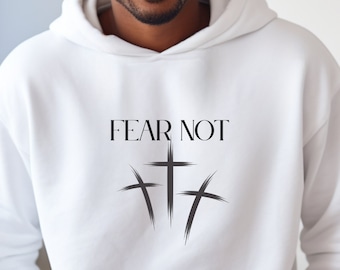 May include: White hoodie with a front pocket and drawstring. The hoodie features the text "FEAR NOT" above three stylized crosses in black. The image shows a person wearing the hoodie.
