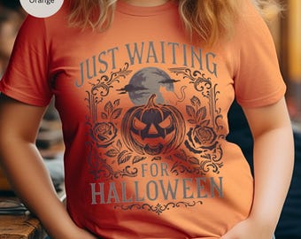 May include: Burnt orange t-shirt with a Halloween-themed graphic. The design features a jack-o'-lantern, full moon, roses, and the text "JUST WAITING FOR HALLOWEEN" in gray lettering. The shirt is short-sleeved.