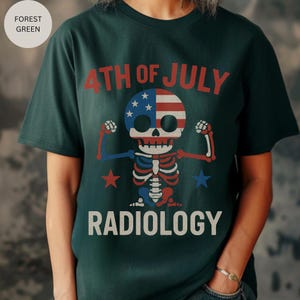 Op de afbeelding: Bosgroen t-shirt met een afbeelding van een skelet met een Amerikaans vlagontwerp op het hoofd, dat zijn armen spant. De tekst "4th of July" en "Radiology" zijn boven en onder het skelet gedrukt.