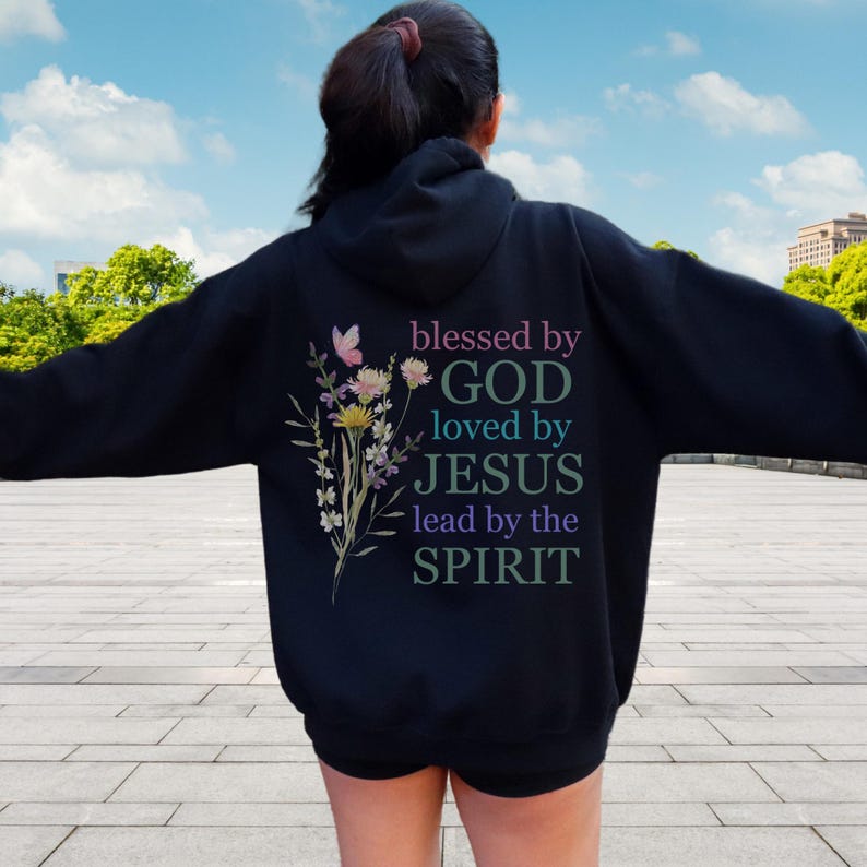 Pu&ograve; includere: Felpa con cappuccio nera con un design floreale e il testo "blessed by GOD loved by JESUS lead by the SPIRIT" stampato sul retro.