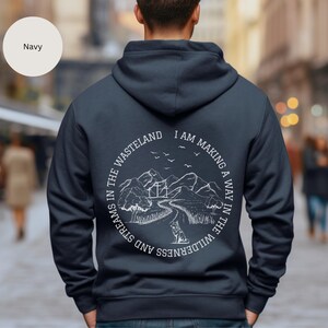 May include: A navy blue hoodie with a white graphic on the back. The graphic features a mountain landscape with a winding path and the text "I am making a way in the wilderness and streams in the wasteland".