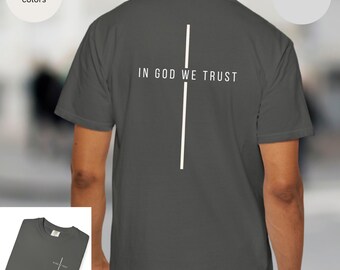 May include: A dark gray t-shirt with the text "IN GOD WE TRUST" and a white vertical line design. The shirt is a comfort colors brand.