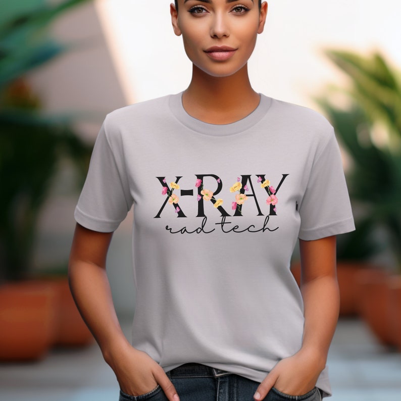 May include: A gray t-shirt with the text "X-RAY rad tech" in black lettering. The letters are decorated with small pink, yellow, and orange flowers.