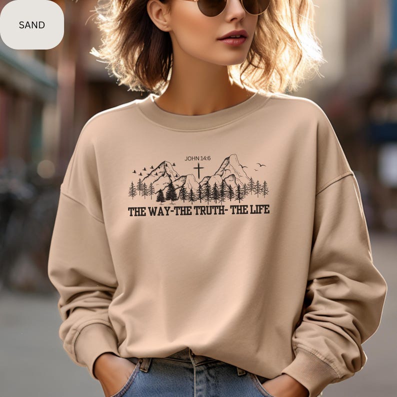 May include: A tan sweatshirt with a mountain scene and a cross. The text "JOHN 14:6" and "THE WAY-THE TRUTH-THE LIFE" are printed on the sweatshirt.