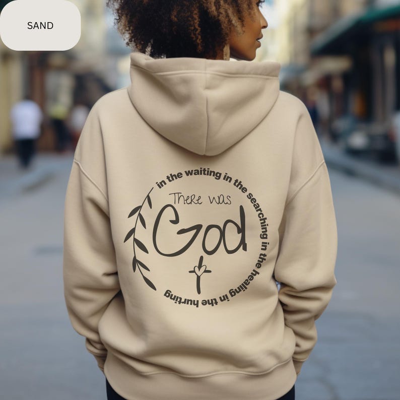 May include: A beige hoodie with a black graphic print on the back. The graphic features a circle with a cross, leaves, and the text "There was God in the waiting in the searching in the healing in the hurting."