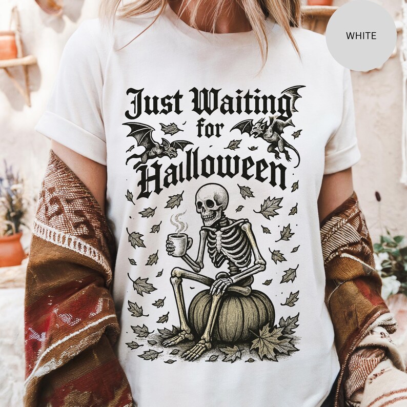 May include: White t-shirt with a Halloween-themed graphic. The design features a skeleton sitting on a pumpkin, holding a mug, with the text "Just Waiting for Halloween" above. Bats and leaves complete the spooky design.