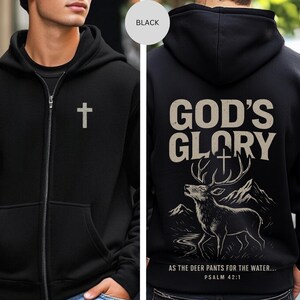 May include: Black zip-up hoodie with a silver cross on the front. The back features the text "GOD'S GLORY" above a deer illustration with mountains and the text "AS THE DEER PANTS FOR THE WATER... PSALM 42:1".