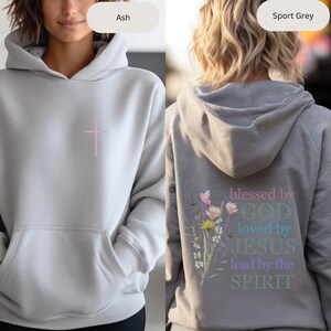 Pu&ograve; includere: Una felpa con cappuccio grigia con una croce rosa sul davanti e il testo "blessed by GOD loved by JESUS lead by the SPIRIT" con accenti floreali sul retro.