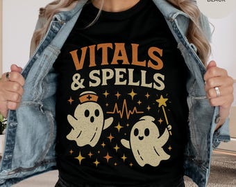 May include: Black t-shirt with the words "VITALS & SPELLS" in orange and white. The shirt features two cartoon ghosts, one wearing a nurse's hat and the other holding a star wand, with a heartbeat line and star accents.