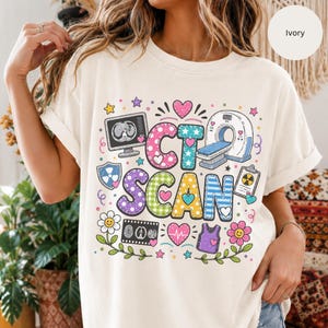 May include: An ivory t-shirt featuring a colorful graphic with the text CT SCAN. The design includes illustrations of a medical scanner, a monitor, a clipboard, a radiation symbol, flowers, and hearts in various patterns like polka dots and stripes.