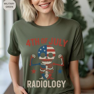 Op de afbeelding: Militairgroen T-shirt met een afbeelding van een skelet met een schedel ontworpen als de Amerikaanse vlag. De tekst "4TH OF JULY" en "RADIOLOGY" zijn in rood en wit gedrukt.