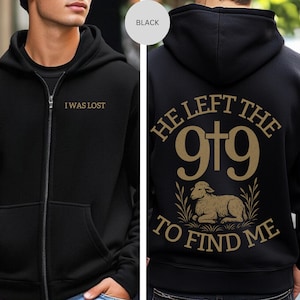 May include: Black zip-up hoodie with the text "I WAS LOST" on the front. The back features the phrase "HE LEFT THE 9+9 TO FIND ME" with a lamb illustration in gold.