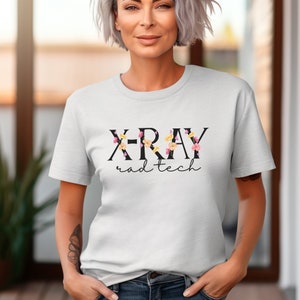 May include: White t-shirt with black text that reads "X-RAY rad tech" with floral accents.