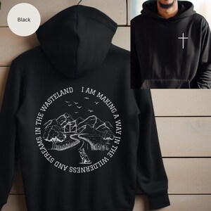 May include: Black hooded sweatshirt with a white graphic design on the back. The graphic features a mountain landscape with a path, trees, and the text "I am making a way in the wilderness and streams in the wasteland".