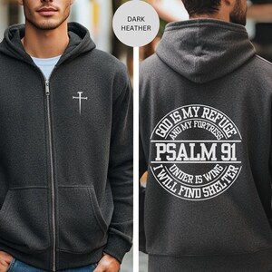 May include: Dark heather grey zippered hoodie with a cross on the front and the text "God is my refuge and my fortress Psalm 91 Under His wing I will find shelter" on the back.