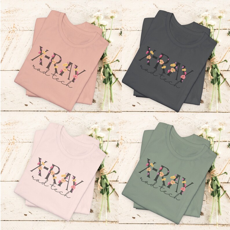 May include: Four folded t-shirts with the text "X-RAY rad tech" in black lettering with floral accents. The shirts are in four colors: pink, gray, light pink, and green.