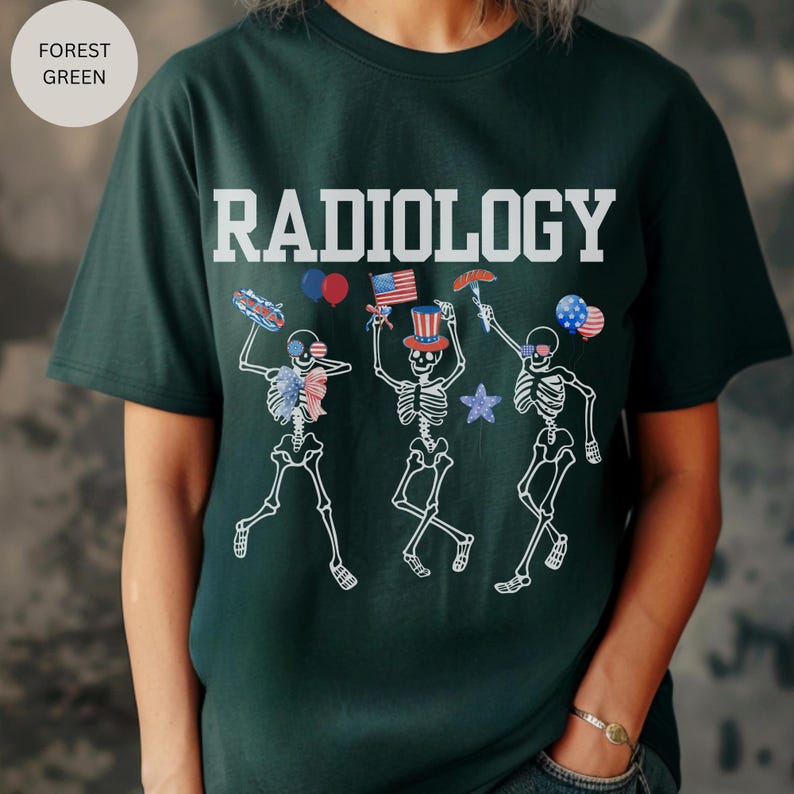 Może przedstawiać: Zielony T-shirt z nadrukiem "RADIOLOGY" w kolorze białym. Trzy szkielety noszą czerwono-biało-niebieskie patriotyczne czapki i trzymają amerykańskie flagi, hot dogi i fajerwerki.