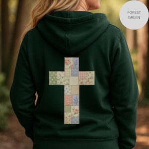 May include: Forest green hoodie featuring a patchwork cross design on the back. The cross is made of various floral and patterned fabric squares in pastel colours. The hoodie has a drawstring hood.