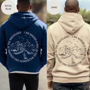 May include: A navy blue and a beige hoodie with a white graphic print on the back. The graphic features a mountain landscape with a winding path, trees, and a wolf. The text on the graphic reads "I am making a way in the wilderness and streams in the wasteland."
