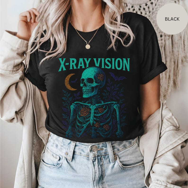 May include: Black t-shirt with the text "X-RAY VISION" above a teal skeleton graphic. The skeleton has roses and is surrounded by leaves and bats. The shirt is a crew neck.
