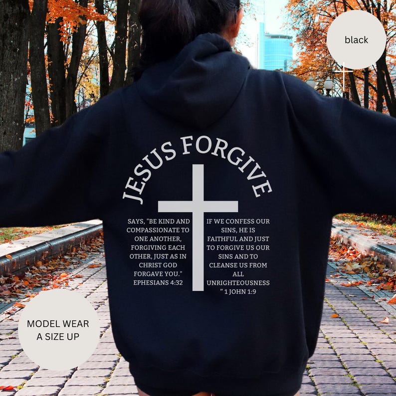 May include: Black hoodie with white text and a cross graphic. The text reads "JESUS FORGIVE" above the cross, with Bible verses below. The hoodie is a size up from the model's usual size.