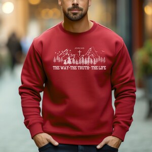 May include: Red sweatshirt with a white graphic of mountains, trees, and a cross. The text "JOHN 14:6 THE WAY-THE TRUTH-THE LIFE" is printed below the graphic.