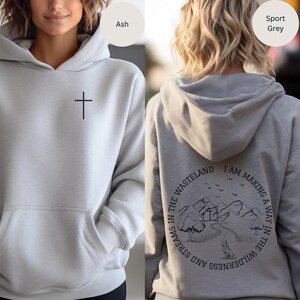 May include: A gray hoodie with a cross on the front and a graphic on the back that says "I am making a way in the wilderness and streams in the wasteland".