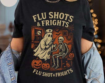 May include: Black t-shirt with a Halloween-themed graphic. The design features a ghost nurse giving a flu shot to a skeleton, with pumpkins and the text "FLU SHOTS & FRIGHTS" and "FLU SHOT & FRIGHTS".