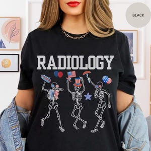 Może przedstawiać: Czarny T-shirt z napisem "RADIOLOGY" w białych literach. Koszulka przedstawia grafikę trzech szkielet&oacute;w ubranych w czerwono-biało-niebieskie patriotyczne stroje, trzymających amerykańskie flagi, hot dogi i balony.