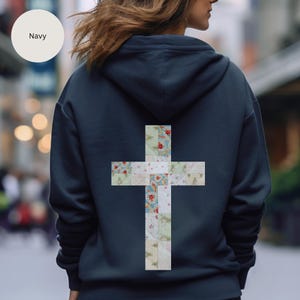 May include: Navy blue hoodie with a large cross design on the back. The cross is made of patchwork fabric with floral and patterned designs in red, blue, and green. The hoodie has a drawstring hood.
