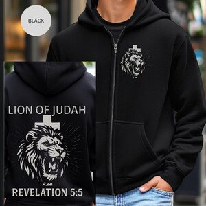 May include: Black zip-up hoodie with a white lion graphic and cross design. The back of the hoodie features the text "LION OF JUDAH" above a lion and cross graphic, with "REVELATION 5:5" below. The hoodie has a hood and front pockets.