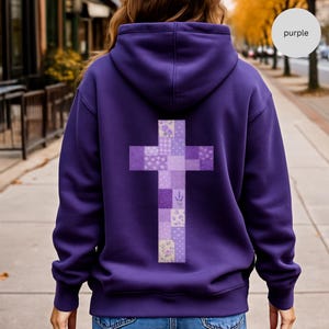 May include: A deep purple hoodie featuring a patchwork cross on the back. The cross is made up of various purple patterned squares, including floral and gingham designs. The word "purple" is in a white circle in the upper right corner.