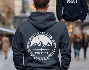 May include: Navy blue hoodie with a white graphic on the back that says "Faithful in Prayer, Be Joyful in Hope, Patient in Affliction, Romans 12:12". The graphic features a mountain range with a crescent moon and stars. The front of the hoodie has the word "Pray" in white.