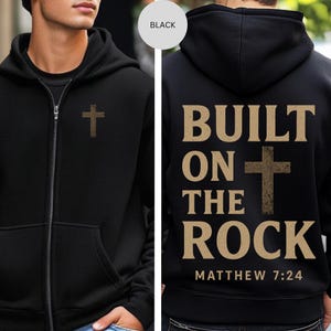 May include: Black zip-up hoodie featuring a small cross on the chest and a larger cross with the text "BUILT ON THE ROCK" and "MATTHEW 7:24" on the back. The hoodie has a hood and a front pocket.