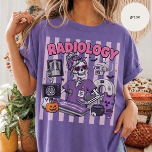 May include: A purple t-shirt with the word "RADIOLOGY" in pink. The graphic shows a skeleton radiologist with heart-shaped sunglasses, medical equipment, a pumpkin, and a ghost.